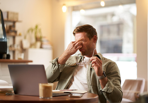 Person rubbing eyes at a laptop, tired from a caffeine crash